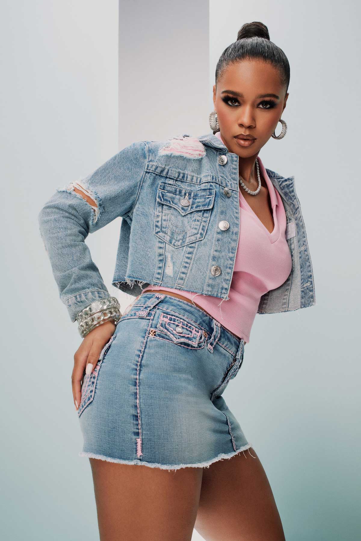 Woman wears a true religion light wash jean jacket and jean skirt with pink stitching, and a pink shirt