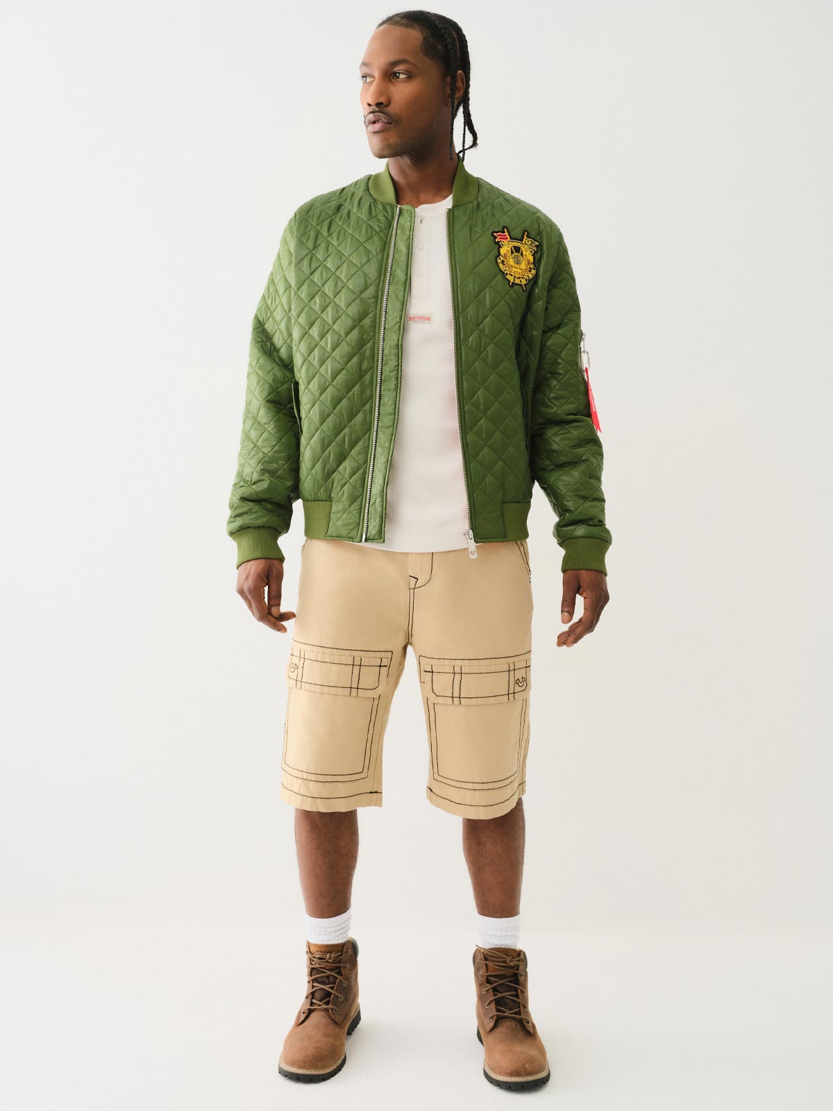 Man wears true religion olive green quilted bomber jacket and true religion tan cargo pants with gray stitching