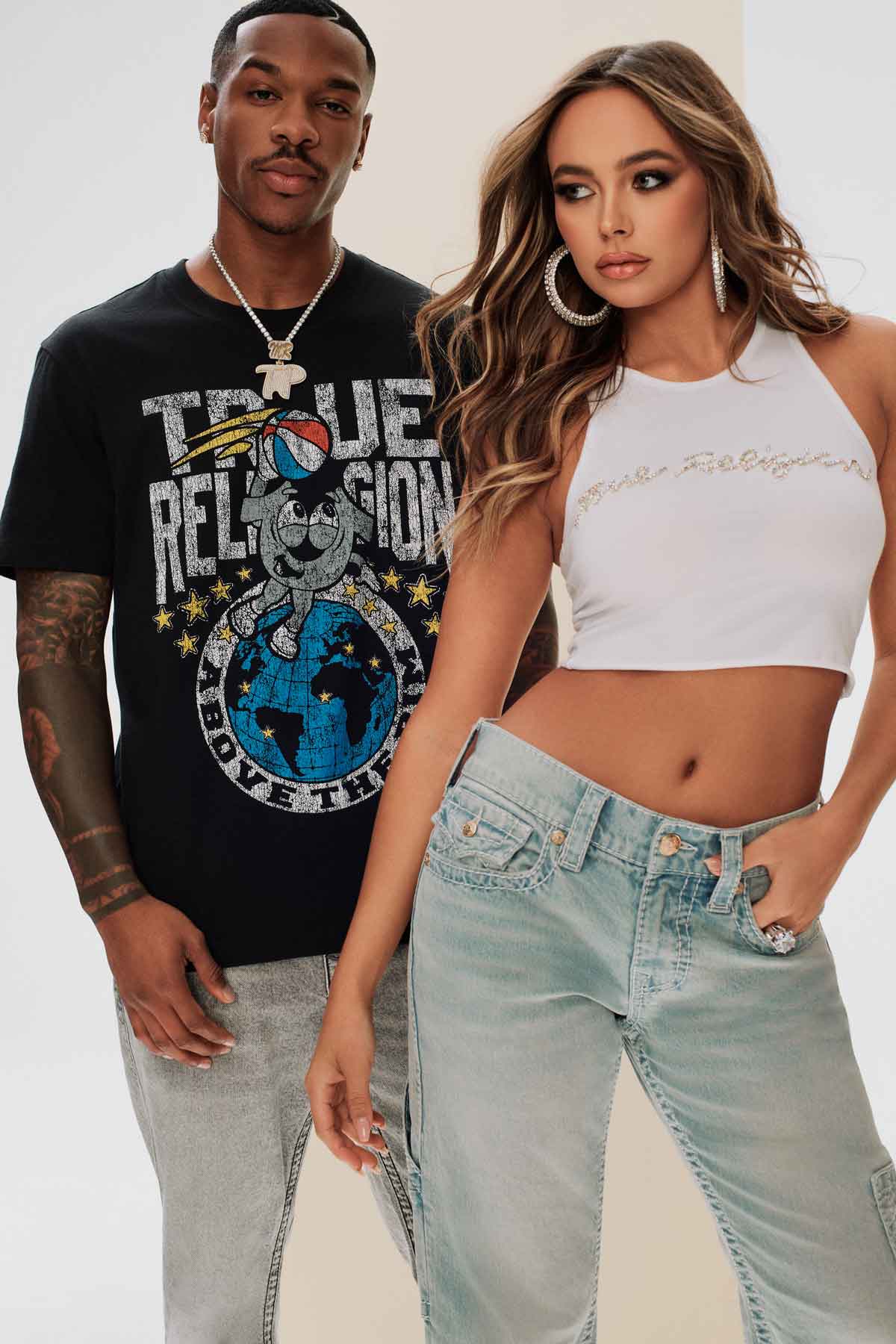 Male model wears true religion black graphic tee and gray jeans, female model wears true religion cropped white tank top and light wash jeans